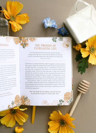 Open book with floral design on a table with flowers and a honey dipper.