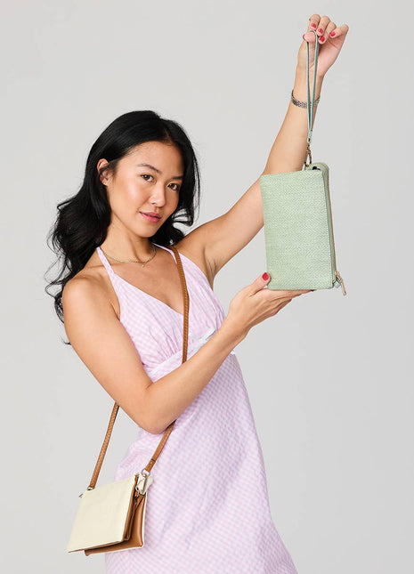 Woman holding a light green crossbody bag against a plain background