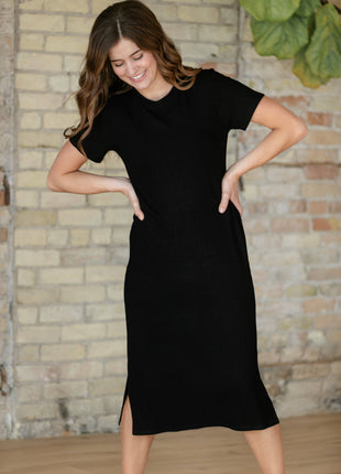 Woman wearing a black dress standing against a brick wall.
