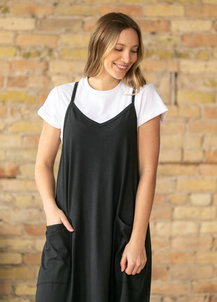 Woman wearing a black slip dress over a white shirt against a brick wall.