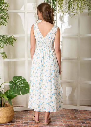 Woman in a floral dress standing in a room with plants and a tiled wall.