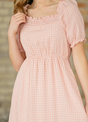 Woman wearing a pink checkered dress with a blurred background